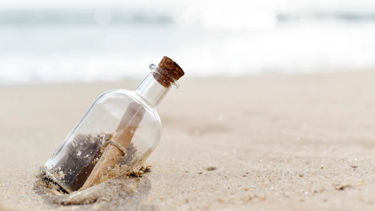 photo of a glass bottle with a scroll inside it sealed with a cork on the beach