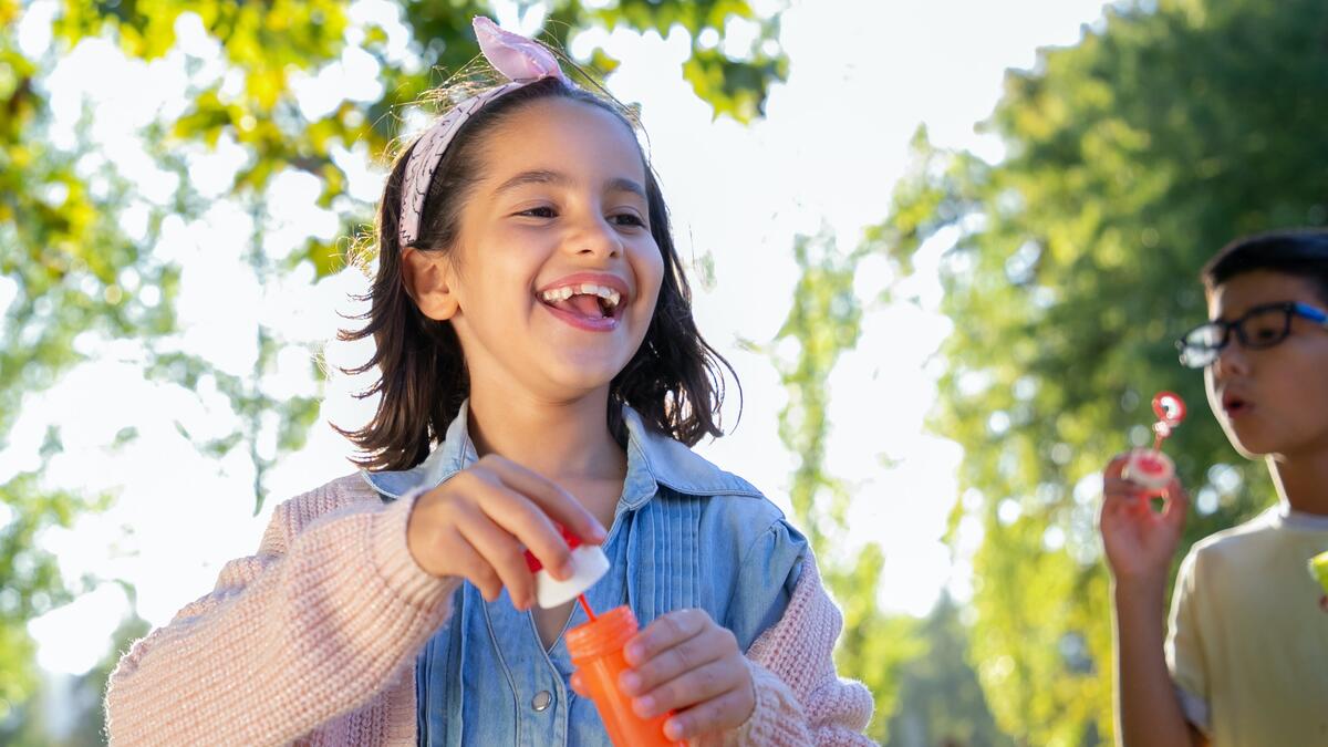 Girl blowing bubbles with trees behind her.