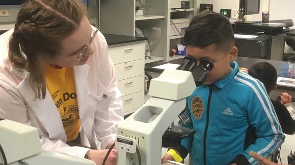 Mentor helping child look through microscope.
