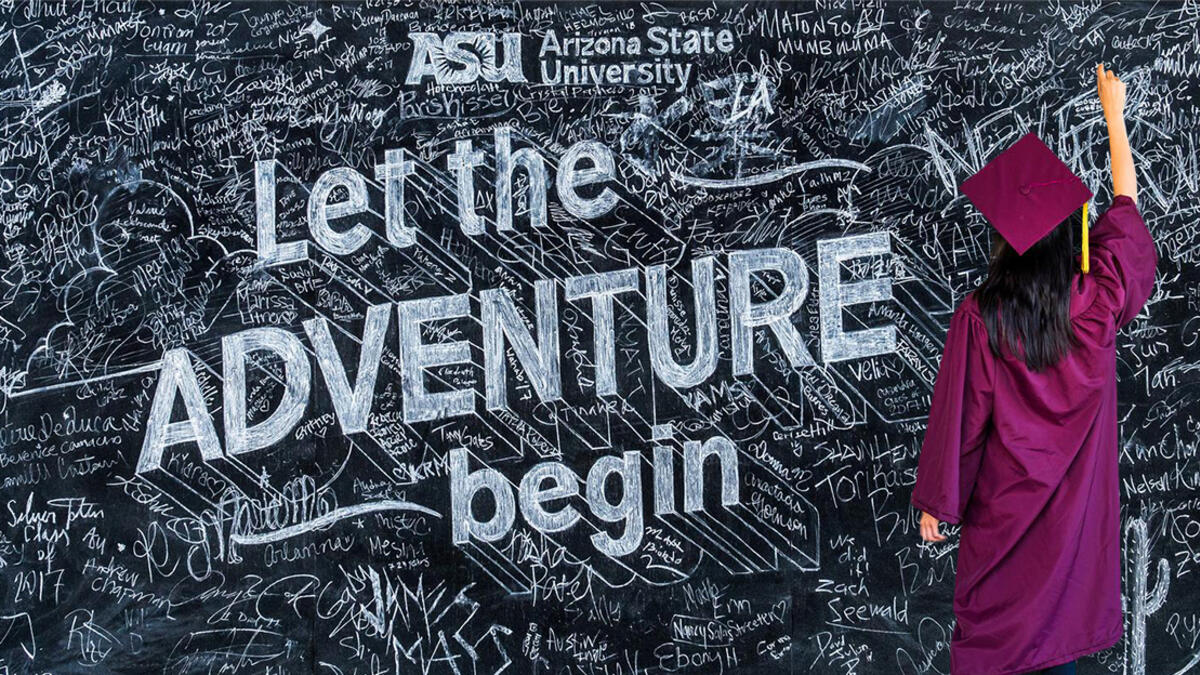 Person with ASU graduation cap and gown writing on a chalkboard